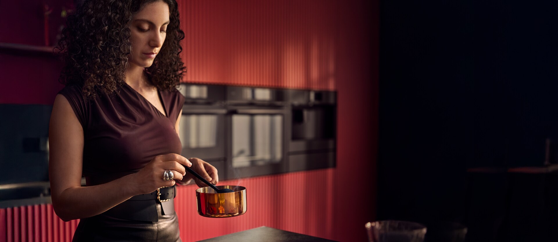 Femme cuisinant dans une cuisine rouge bordeaux où des casseroles sont posées sur une plaque à induction AEG.